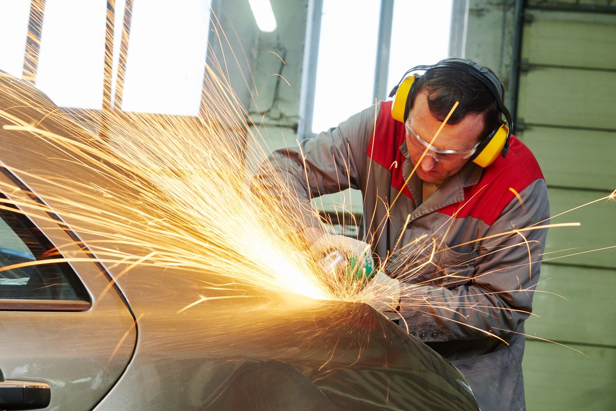 Technician cutting a damaged panel with a cut off tool during structural repair