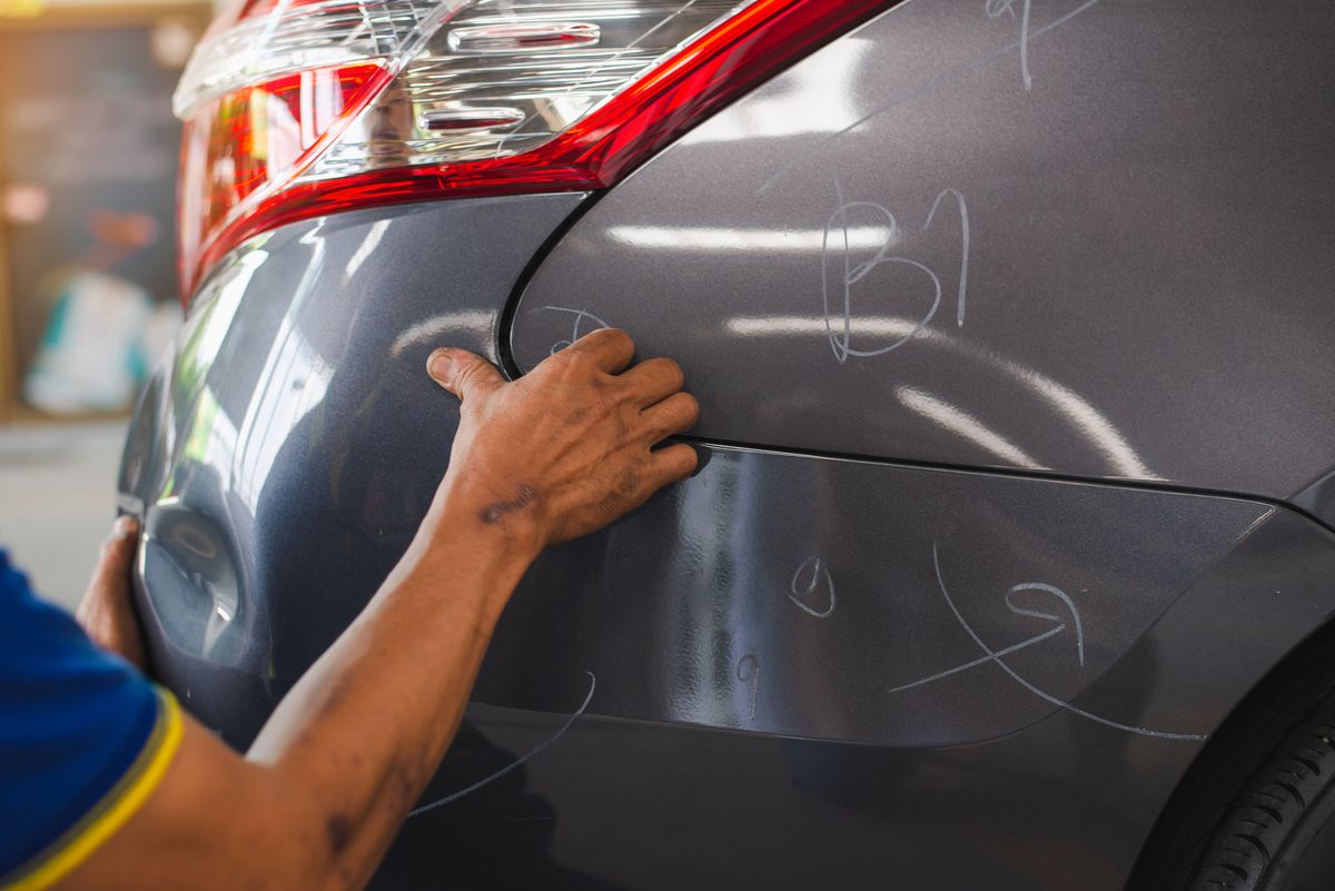 Technician assessing dents on a rear quarter panel under directional light